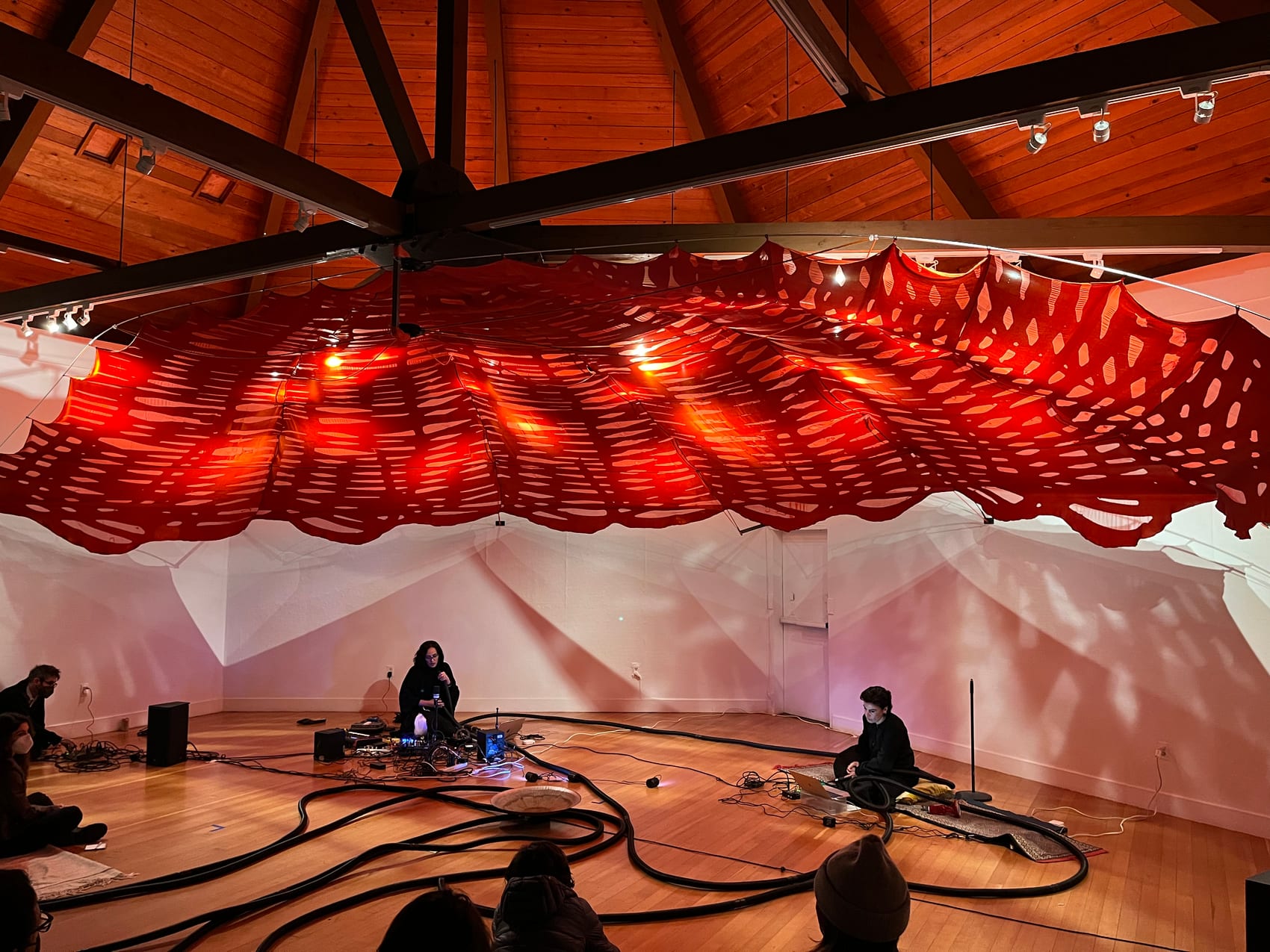 A glowing red suspended form fills a domed performance space, with the audience seated below — Crossings / عبور