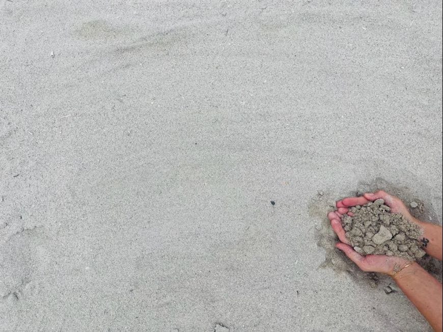 Two hands cradling a handful of earth on pale sand — Love Letters to Palestine