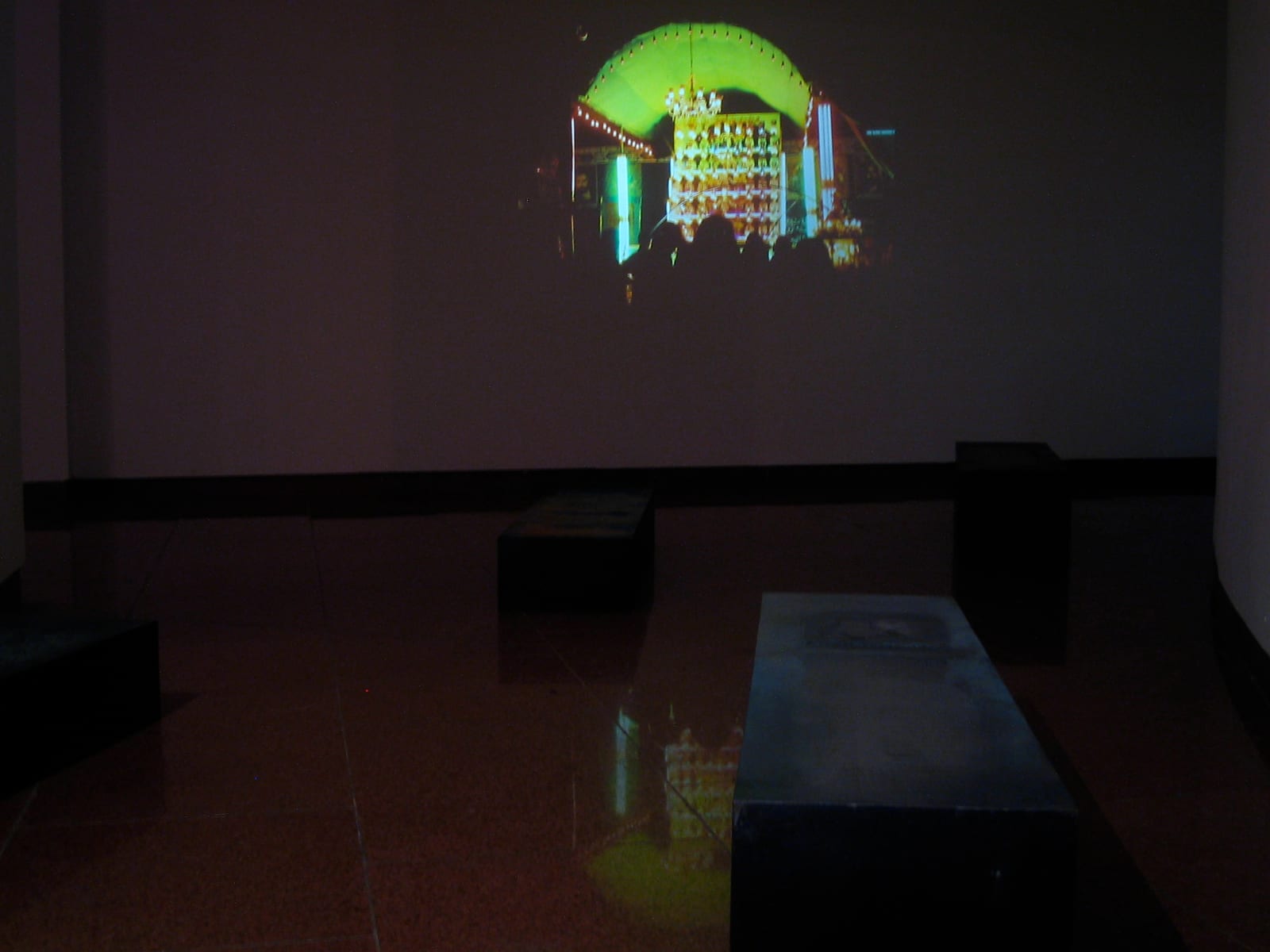 A gallery installation: a low vitrine before a glowing green-lit alcove — Sacred Spaces